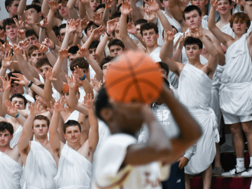 A basketball player takes a shot with an army of fans dressed for a toga party cheering him on